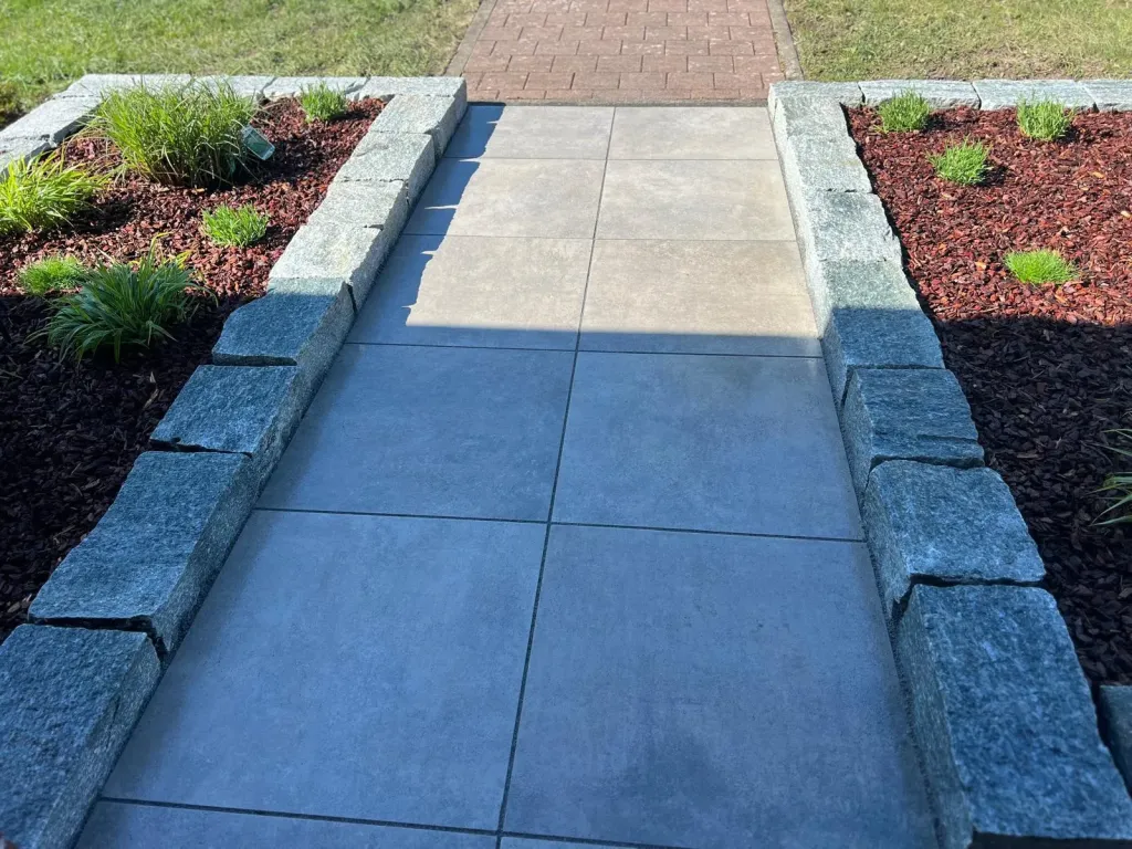 Gartenweg aus großen Betonplatten zwischen Granitmauern