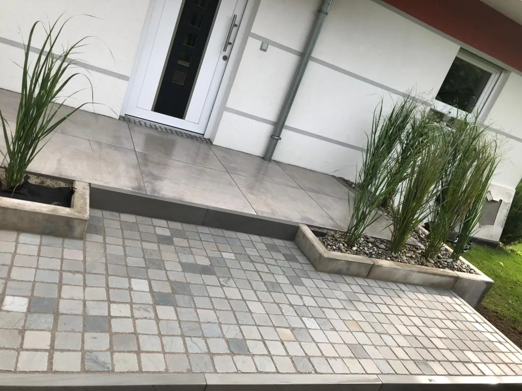 Gepflasterter Vorplatz mit Ziergräsern vor einem weißen Haus