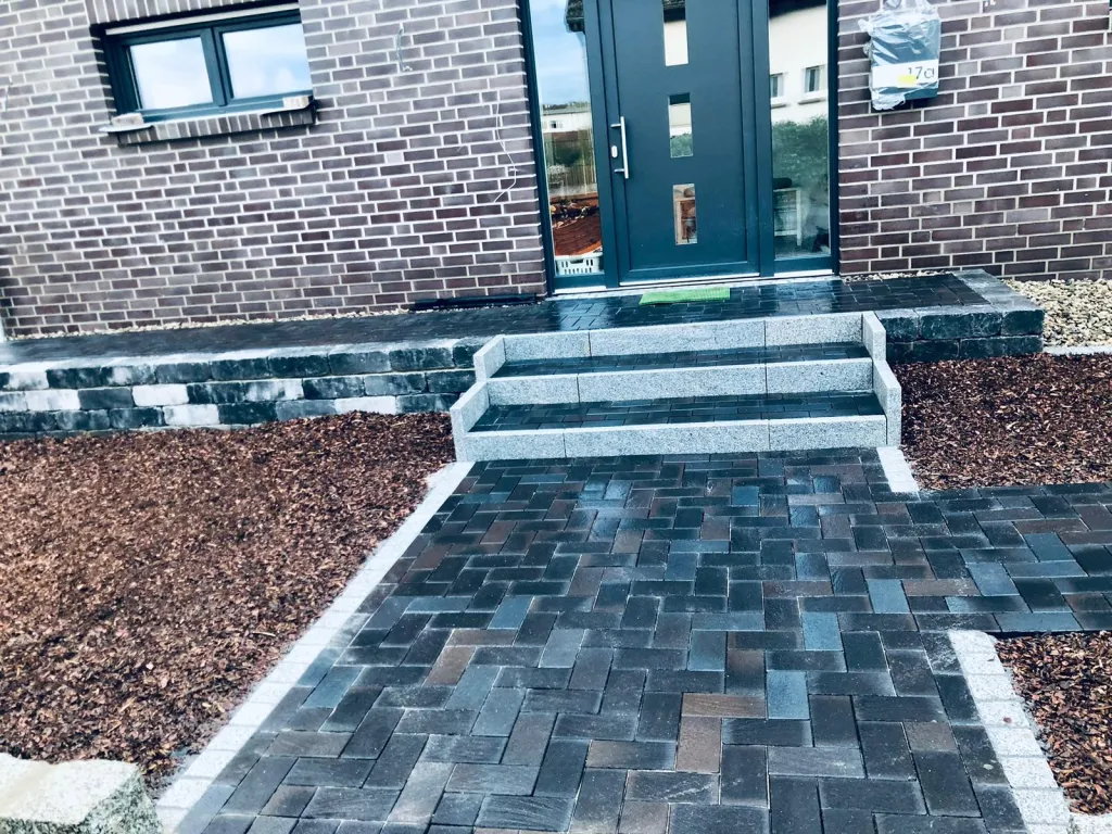 Hauszugang aus dunklem Pflaster mit Mulchbeeten