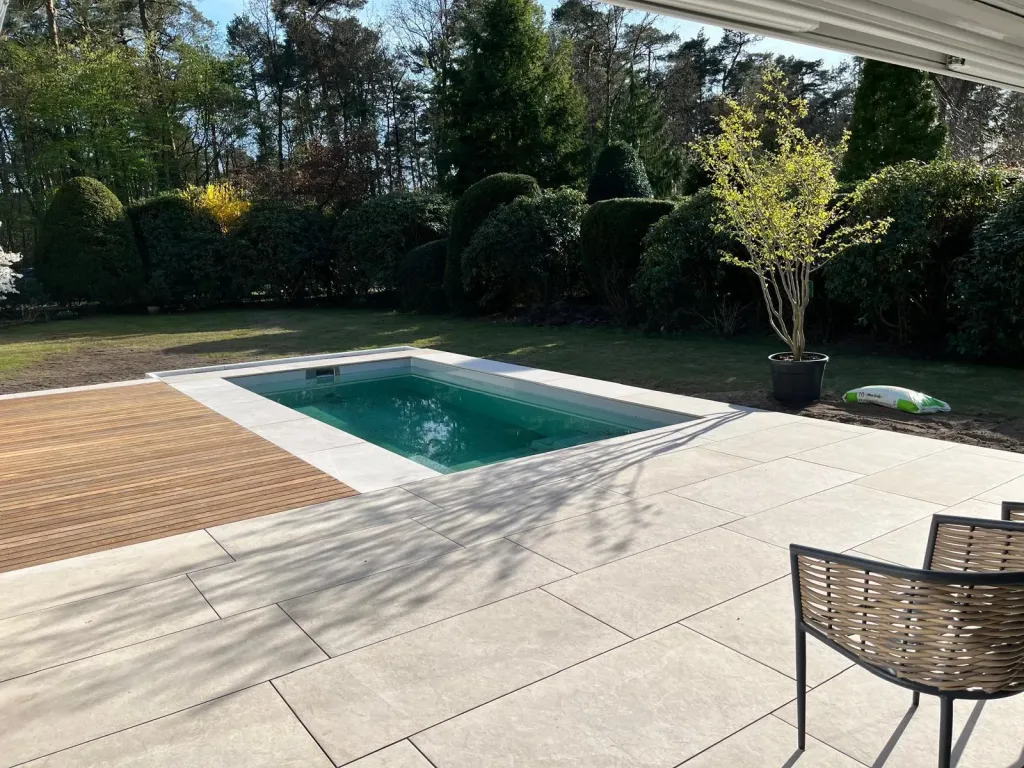 Kleiner Pool mit heller Plattenumrandung vor Hecken