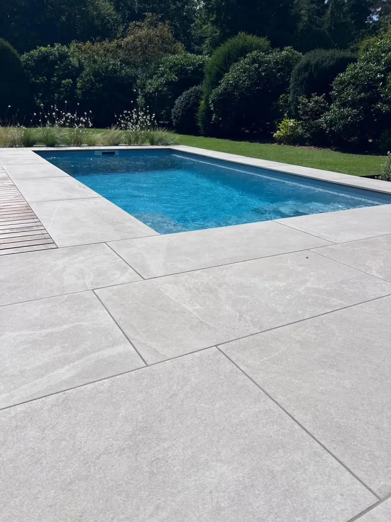 Pool mit heller Plattenumrandung und Heckenkulisse