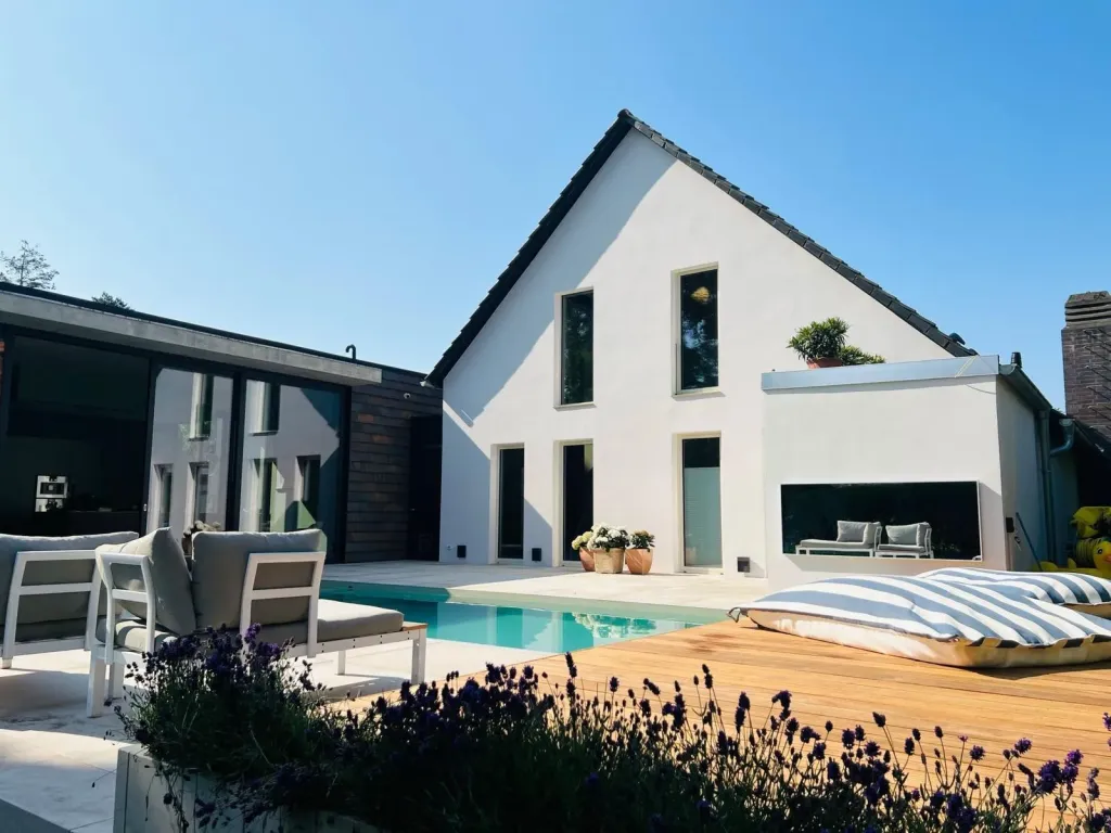 Poolgarten mit Holzdeck und Lavendel vor einem weißen Einfamilienhaus