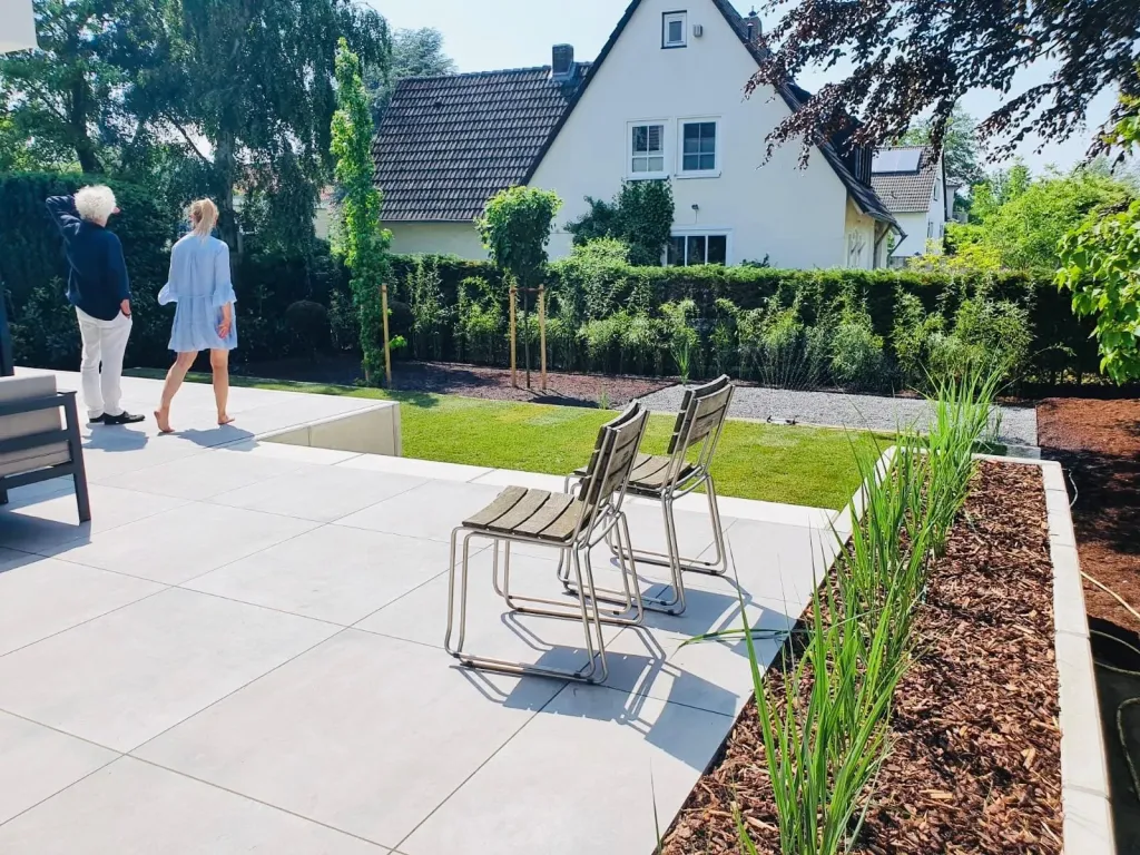 Terrasse aus großen hellen Platten mit Gartenstühlen