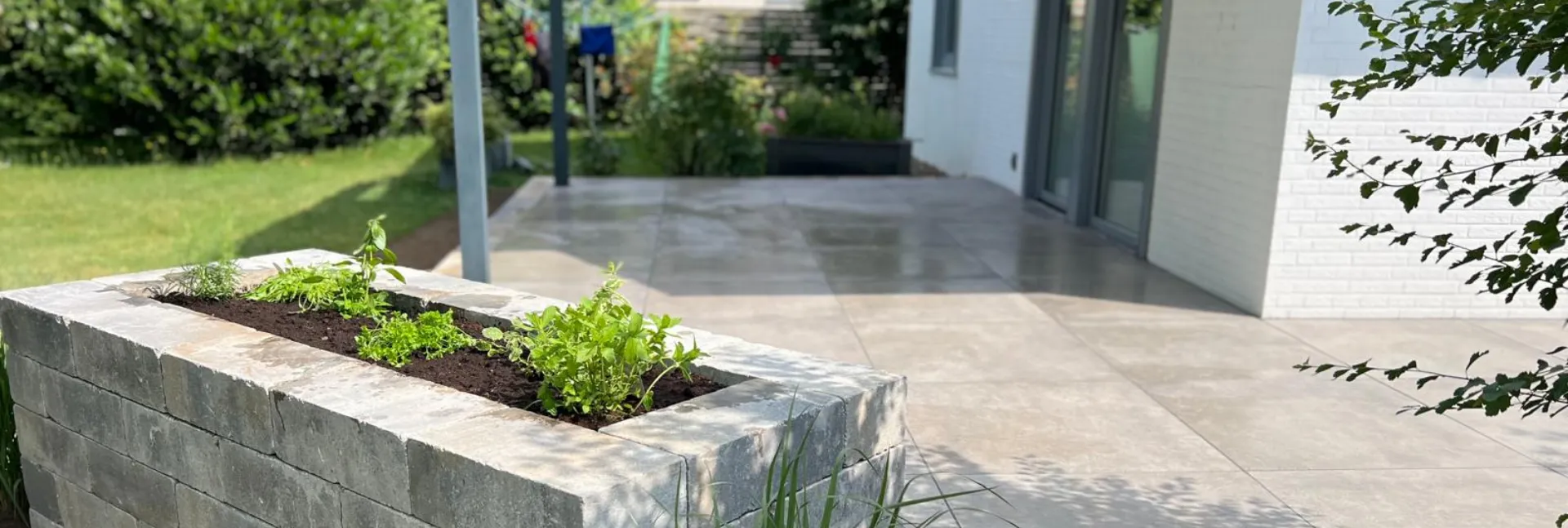 Terrasse aus hellen Natursteinplatten mit Hochbeet vor modernem Haus